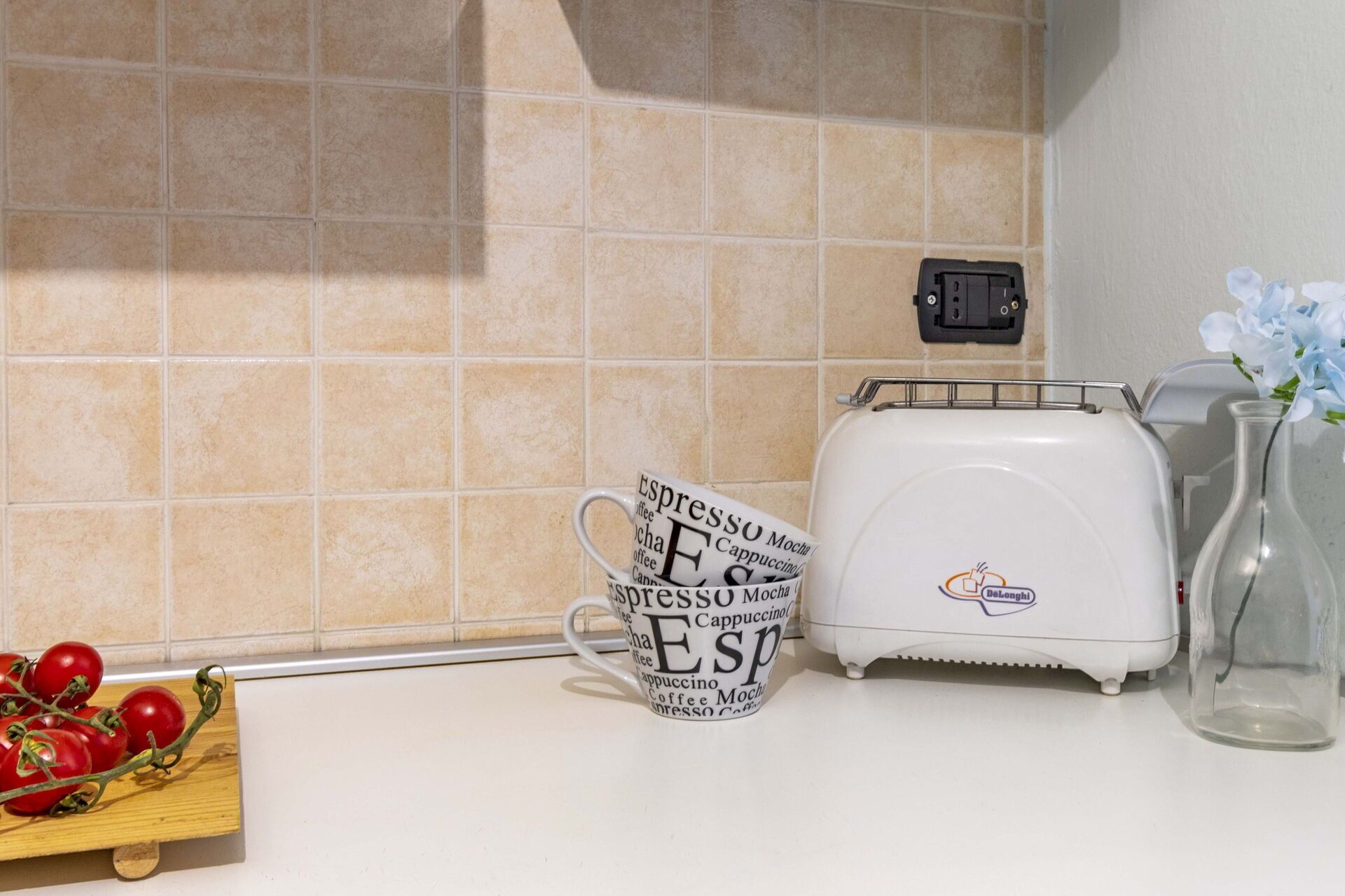 A kitchen counter with a coffee maker, a mug with coffee-related words, and a wooden board with tomatoes.