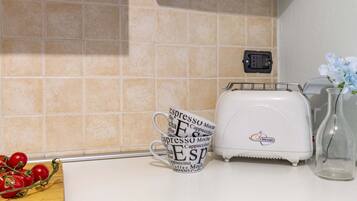 A kitchen counter with a coffee maker, a mug with coffee-related words, and a wooden board with tomatoes.
