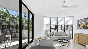 A modern living room with a sofa, coffee table, and a view of a patio area with outdoor furniture. - Modern 2 Bedroom Apartment in Broadbeach - Q Stay (Gallery 206 - 2N - NB) (Broadbeach)