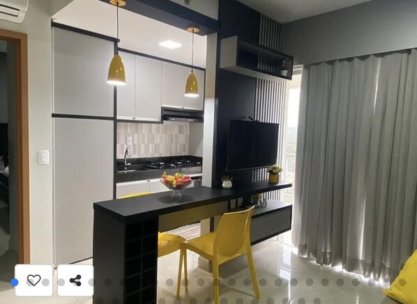 A modern kitchen with a central island, a flat-screen TV, and yellow chairs.