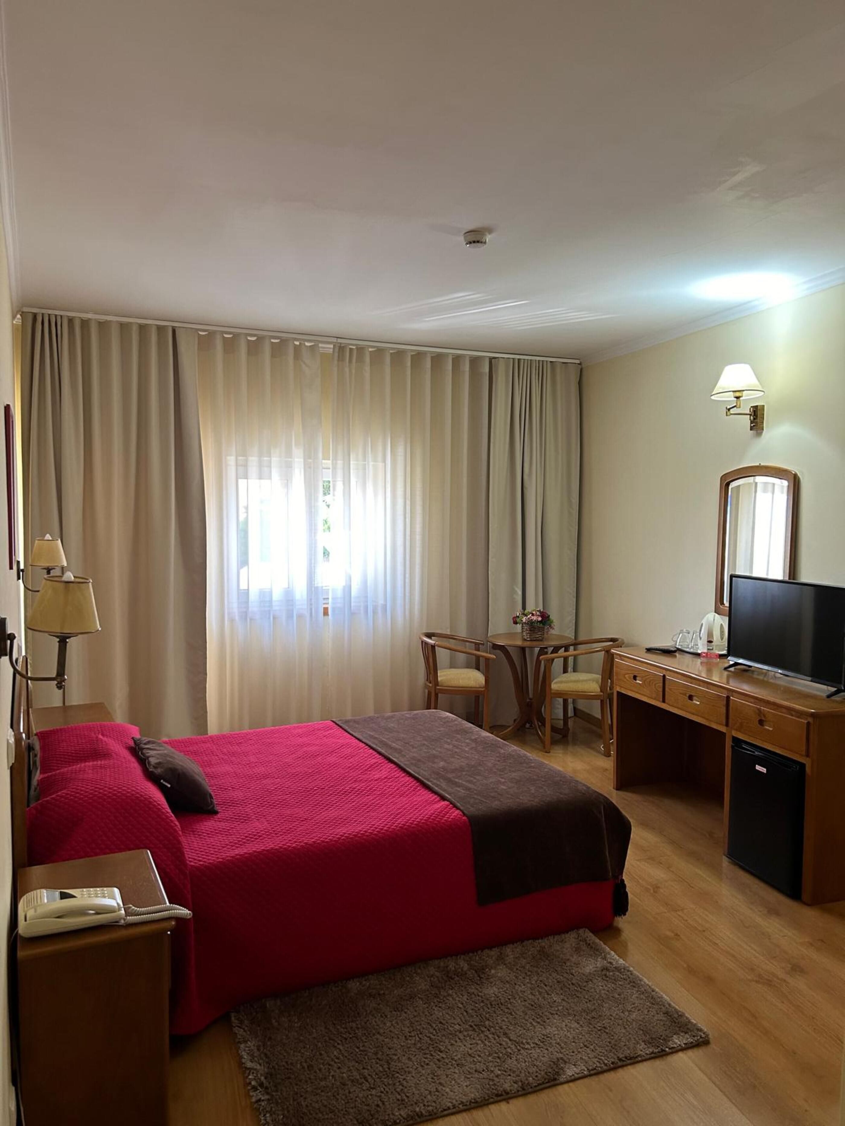 A hotel room with a bed, desk, chair, television, and a telephone.