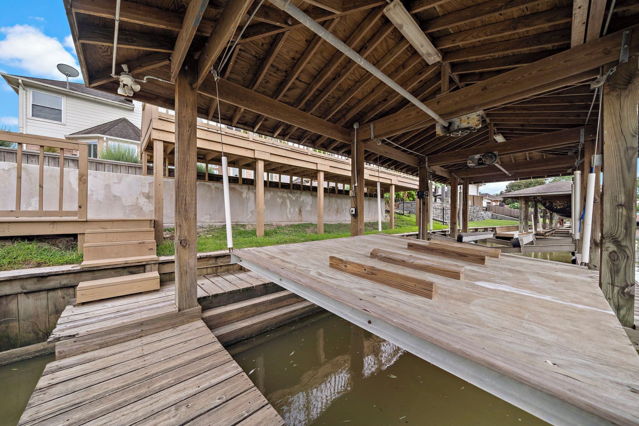A wooden deck with a metal roof, a small pool, and a house in the background.