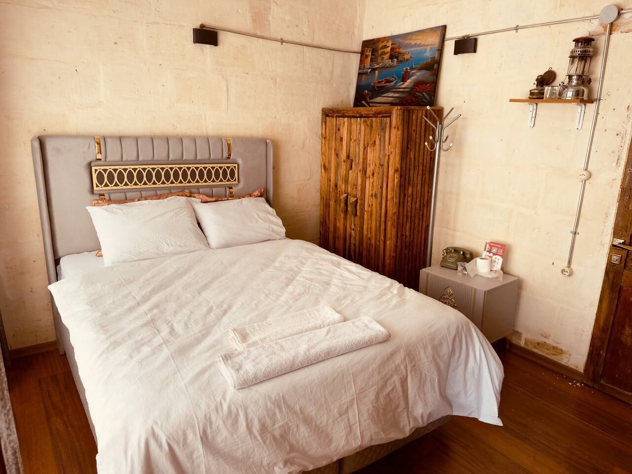 Un letto rifatto con lenzuola bianche, una testiera in legno e un quadro appeso sopra.