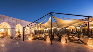An outdoor seating area with tables and chairs, a canopy structure, and a building with arched windows in the background. - Fazilet Hanım Konağı (Gaziantep)