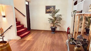 A spacious room with a wooden floor, a red staircase, a potted plant, and a shelf with various items. - Fazilet Hanım Konağı (Gaziantep)