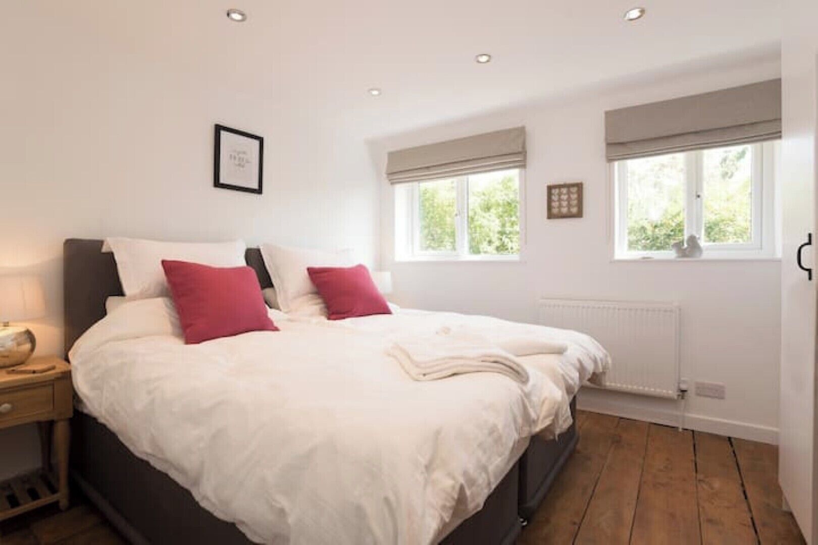 A bedroom with a large bed, two bedside tables, a window with blinds, and a radiator.
