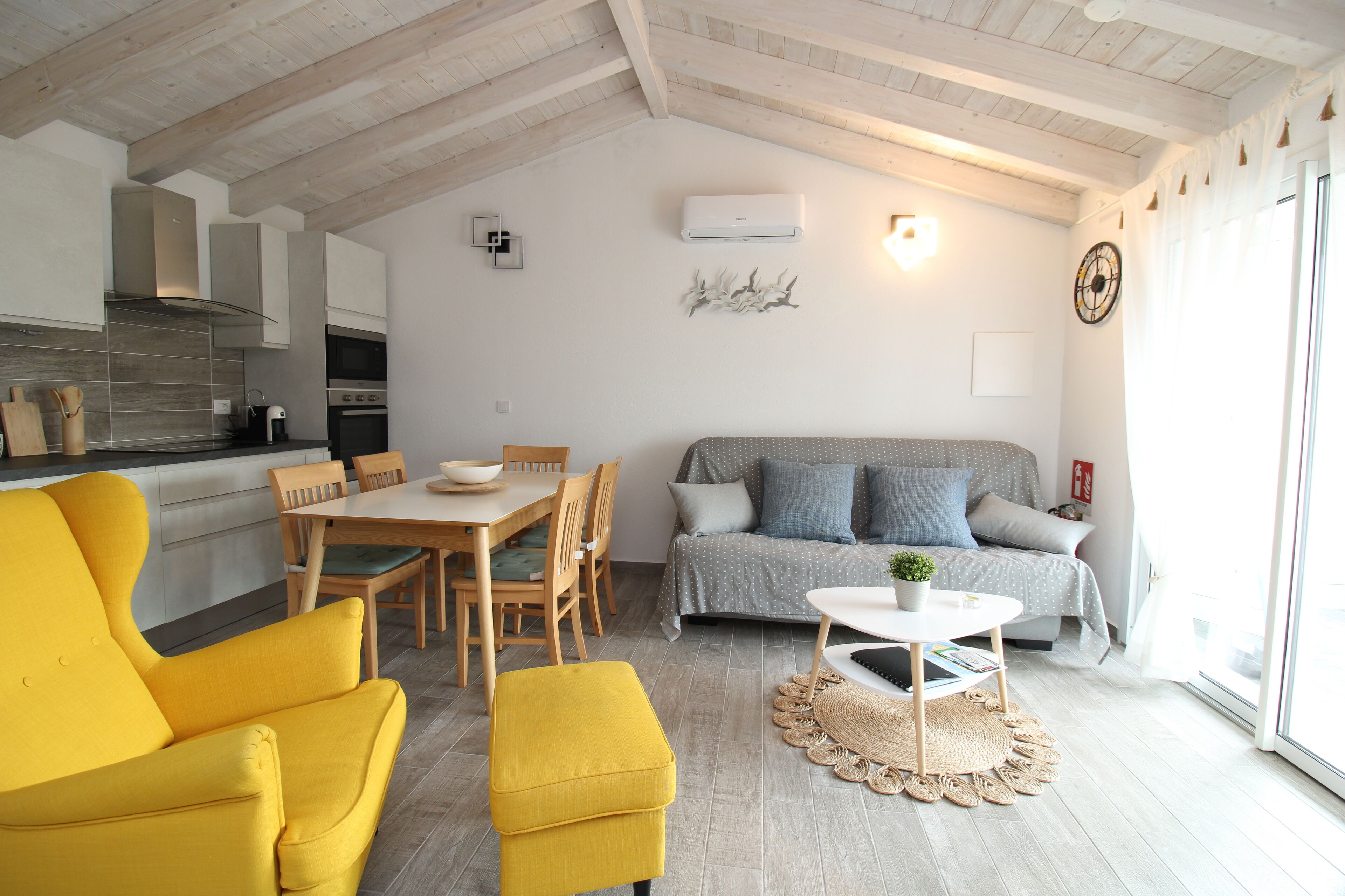 Ein modernes Wohnzimmer mit einem gelben Sessel, einer Couch, einem Esstisch mit Stühlen und einem kleinen Couchtisch.