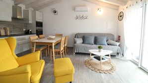 A modern living room with a yellow armchair, a sofa, a dining table with chairs, and a small coffee table. - Arena's Casa Vacanze (La Caletta)