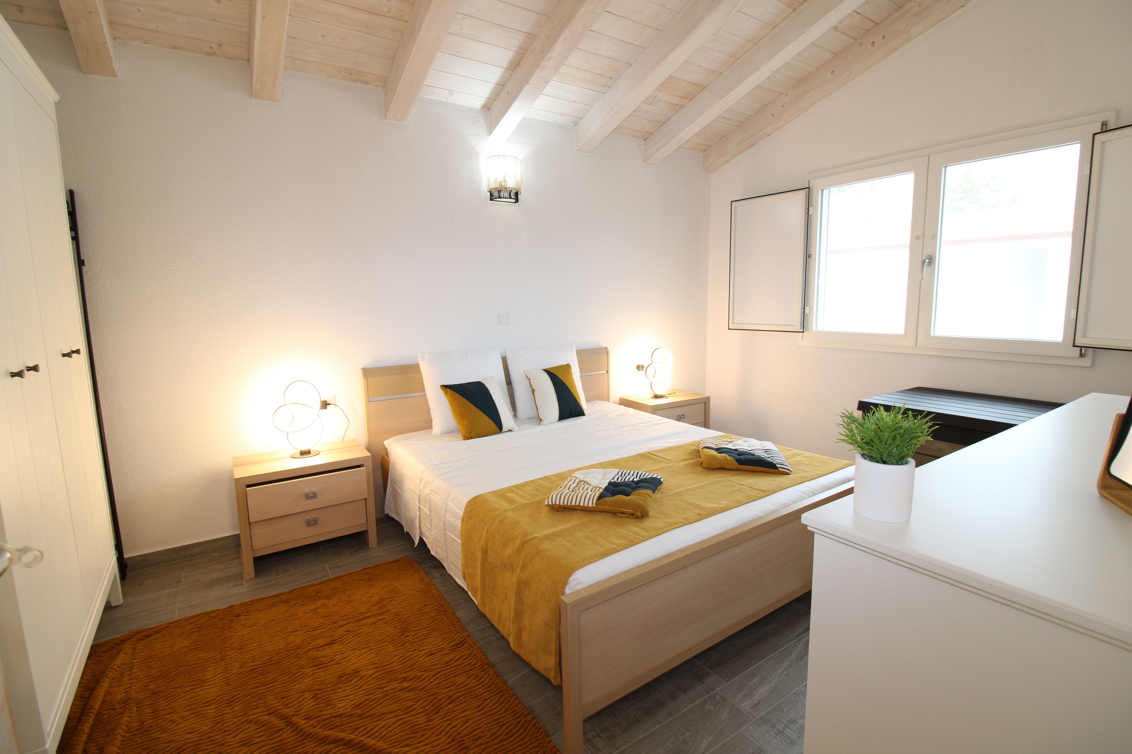 Ein Schlafzimmer mit Bett, Nachttischen, Schreibtisch, Fenster und Deckenleuchte.