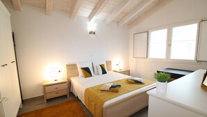 A bedroom with a bed, bedside tables, a nightstand, a desk, a window, and a ceiling light. - Arena's Casa Vacanze (La Caletta)