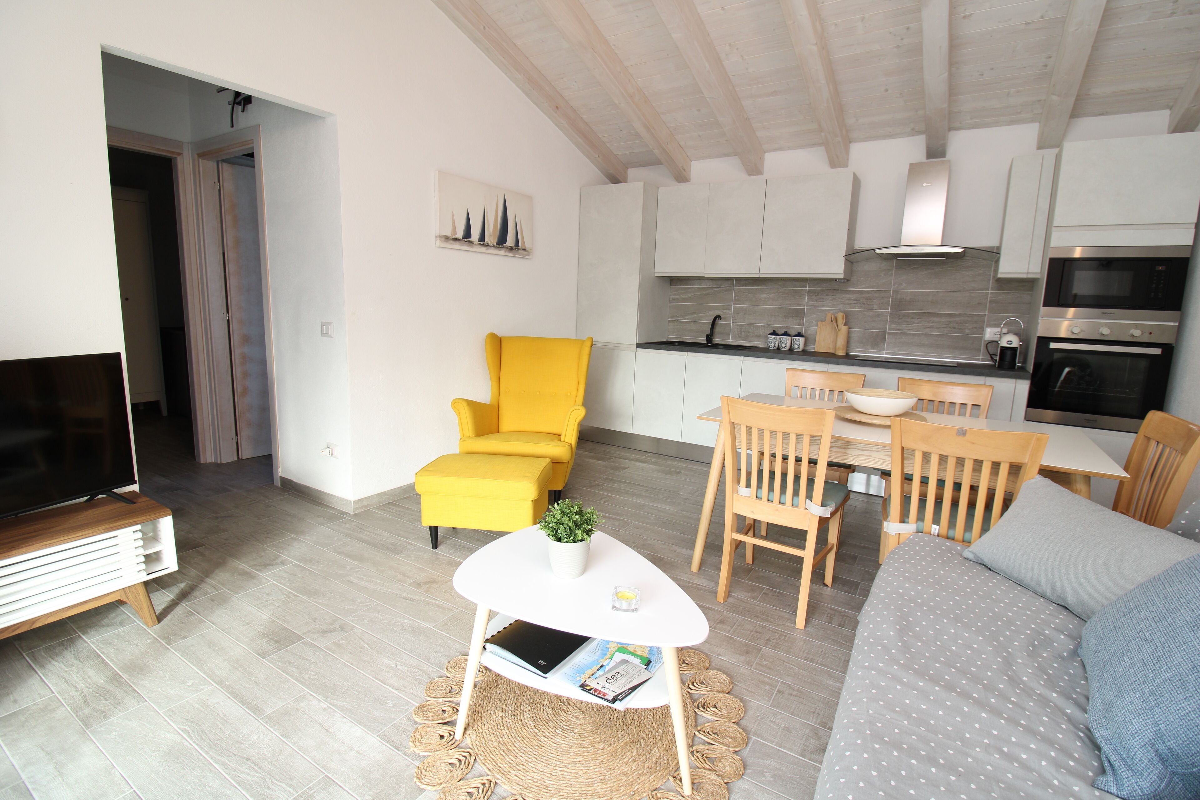 Ein modernes Wohnzimmer mit einer Couch, einem gelben Sessel, einem kleinen Tisch mit Pflanze und einem Fernsehschrank.
