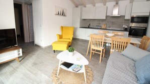 A modern living room with a sofa, a yellow armchair, a small table with a plant, and a TV stand. - Arena's Casa Vacanze (La Caletta)