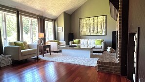 A spacious living room with hardwood flooring, a white sofa, a beige sofa, and a large painting of a forest on the wall.