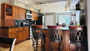 A modern kitchen with wooden cabinets, a microwave, a stove, and bar stools.