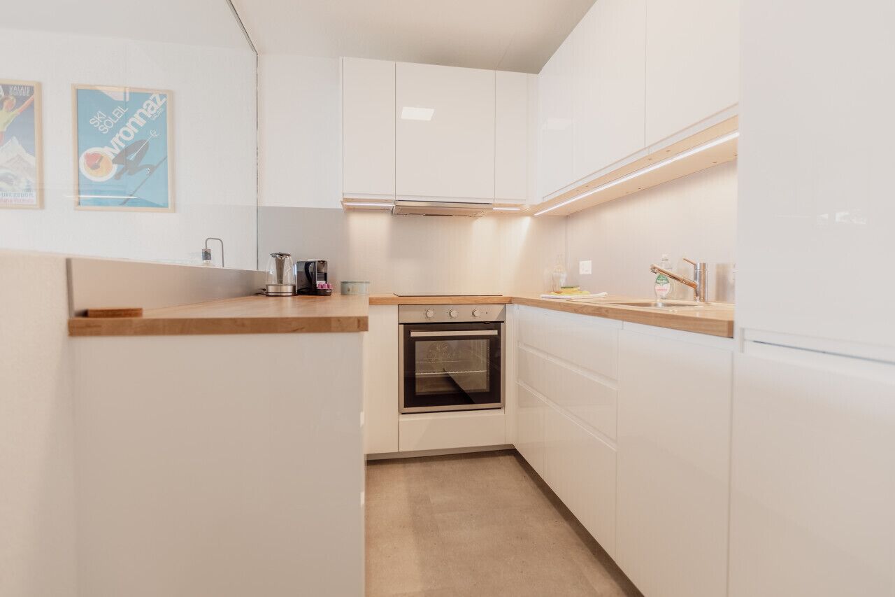 A compact kitchen with white cabinets, a built-in oven, and a wooden countertop.