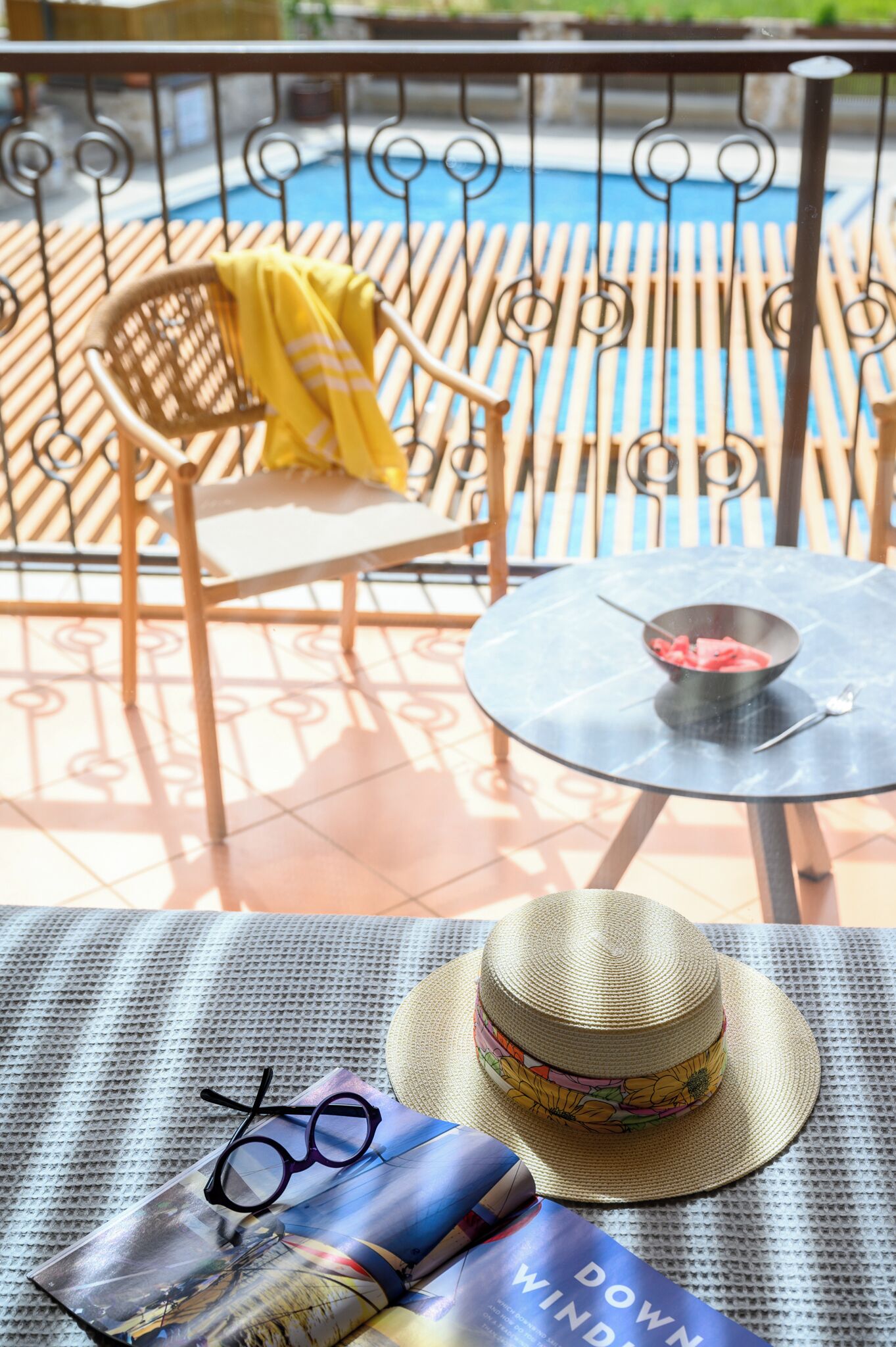 A poolside area with a wicker chair, a round table with a bowl, and a hat on a mat.