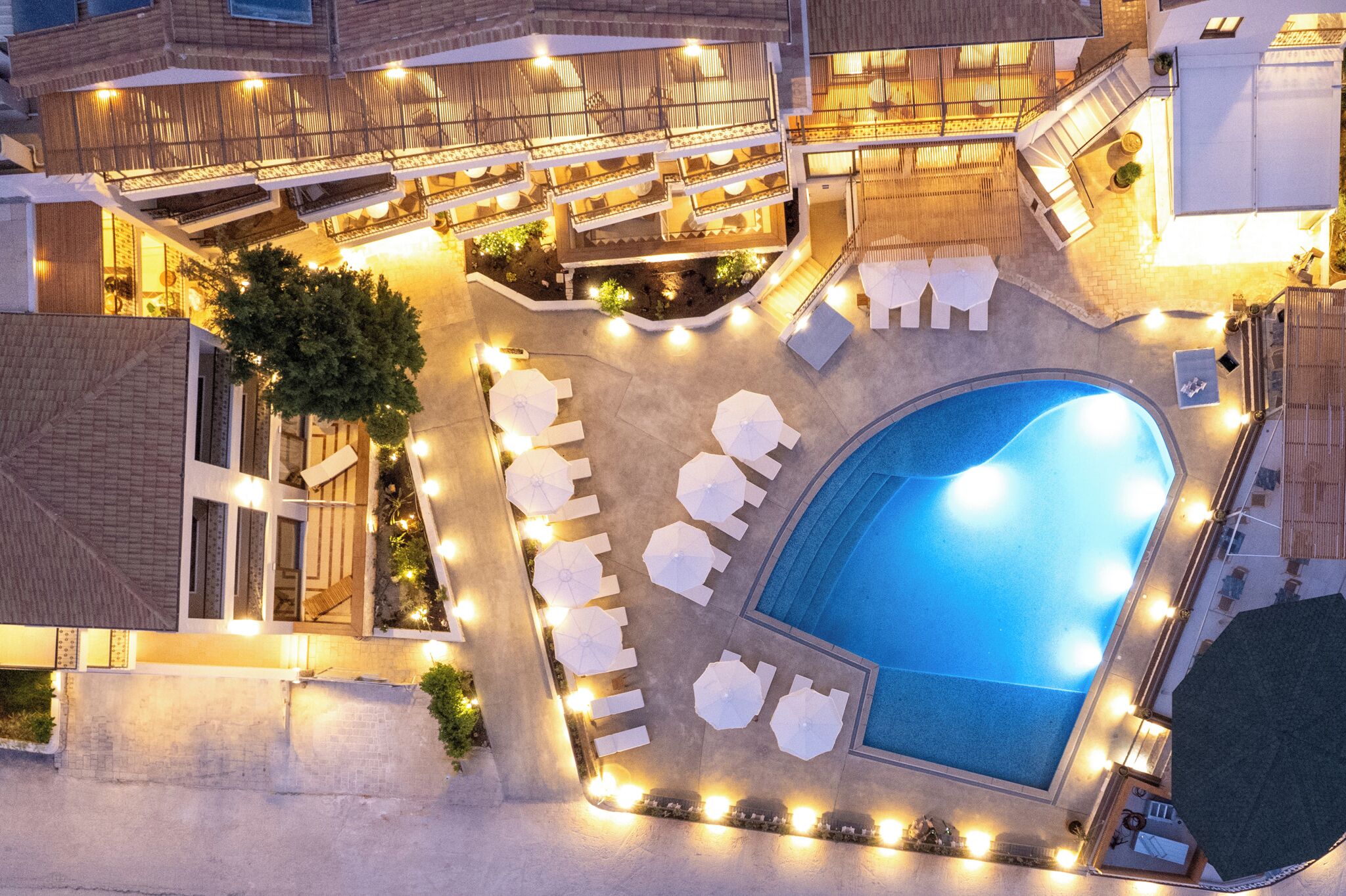 Vista aerea di un hotel con piscina, numerosi balconi e aree salotto all'aperto.