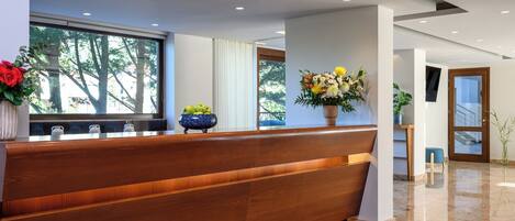 Un área de recepción con un banco de madera, un ventanal grande y plantas en macetas.