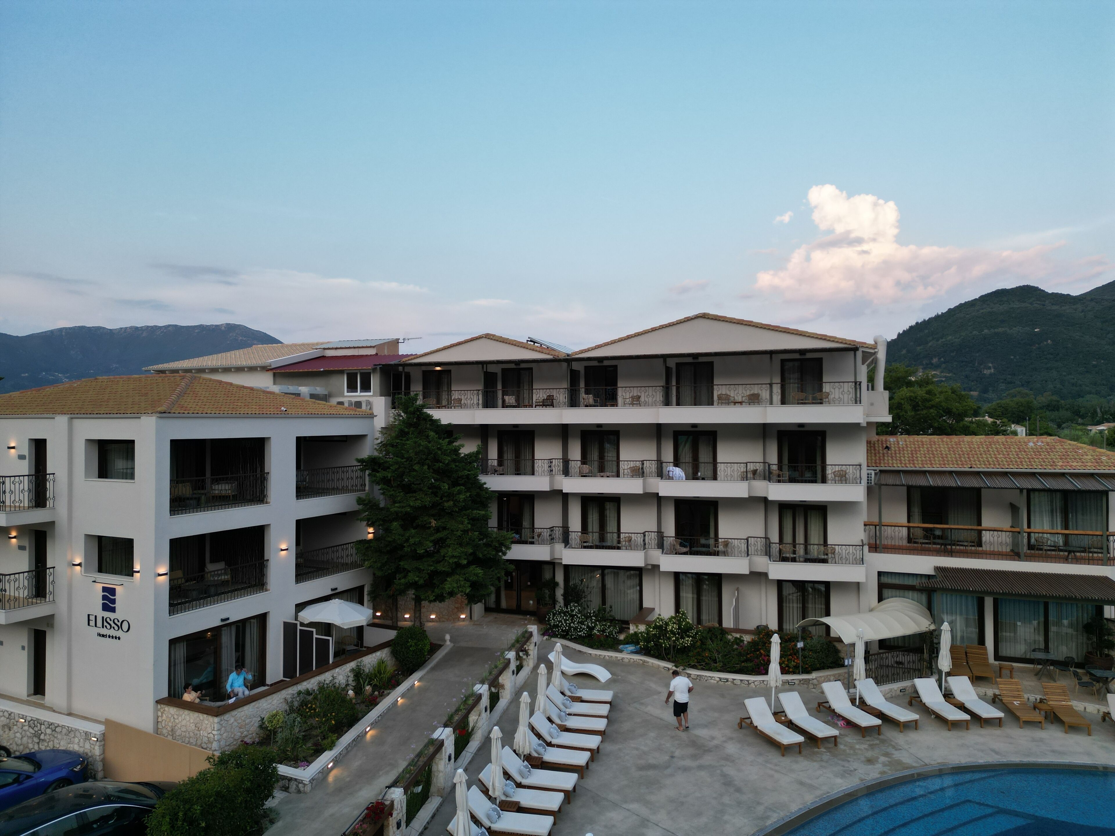 A hotel with multiple balconies, a swimming pool, and a view of mountains.