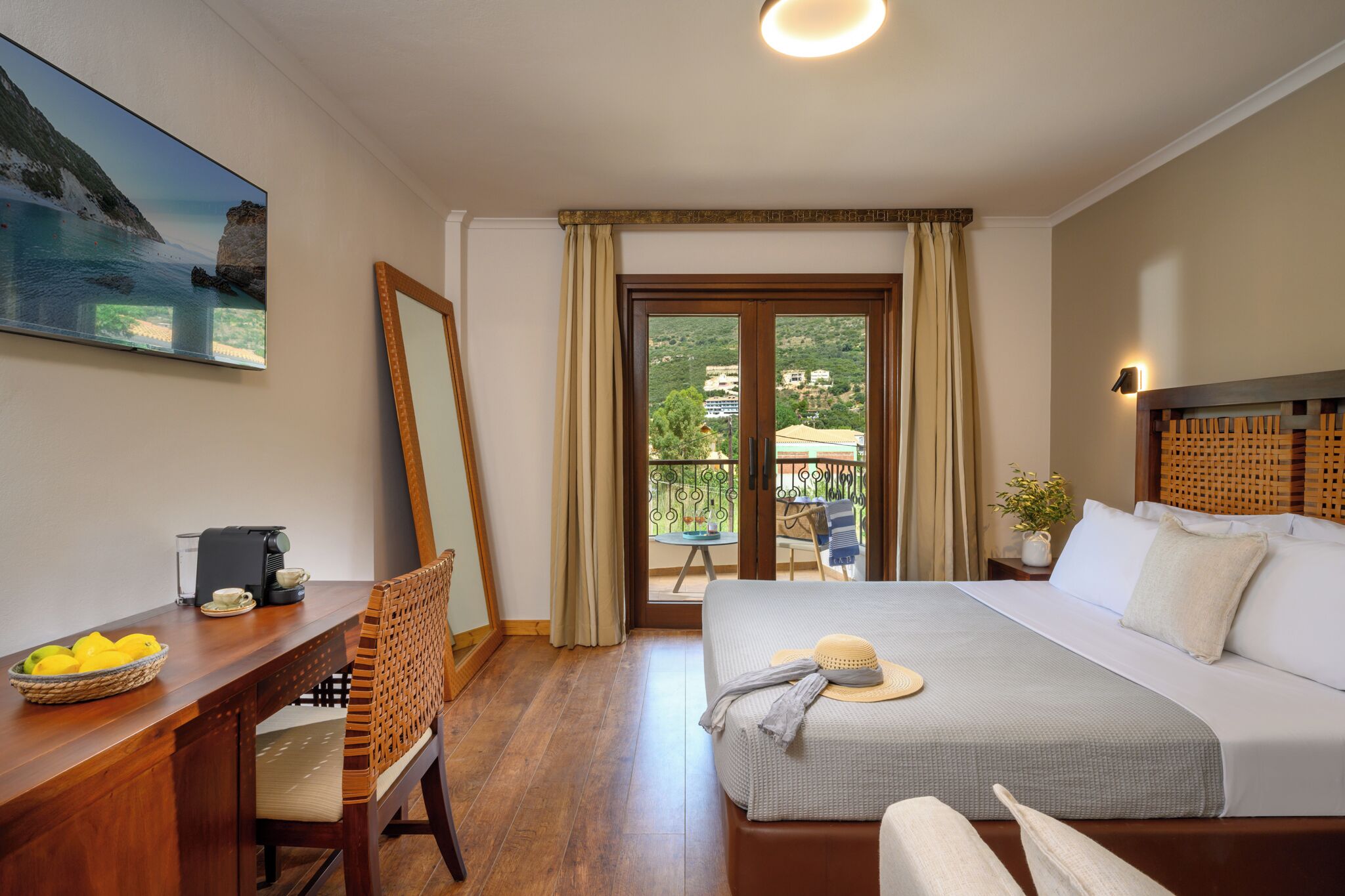 A hotel room with a bed, a desk with a coffee maker, a chair, a dining table, and a balcony with a view of the sea.