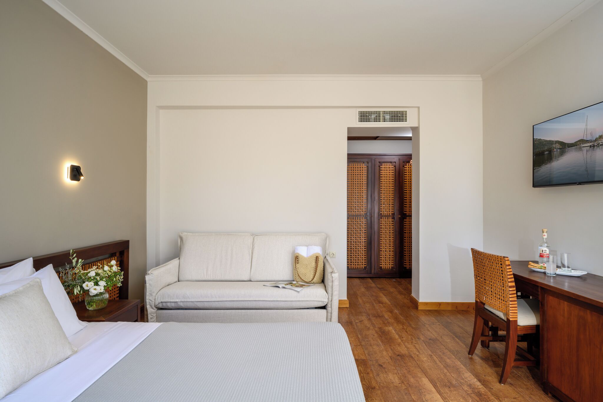 A hotel room with a bed, a sofa, a desk, and a chair. There is a painting on the wall and a window with a view of the outside.