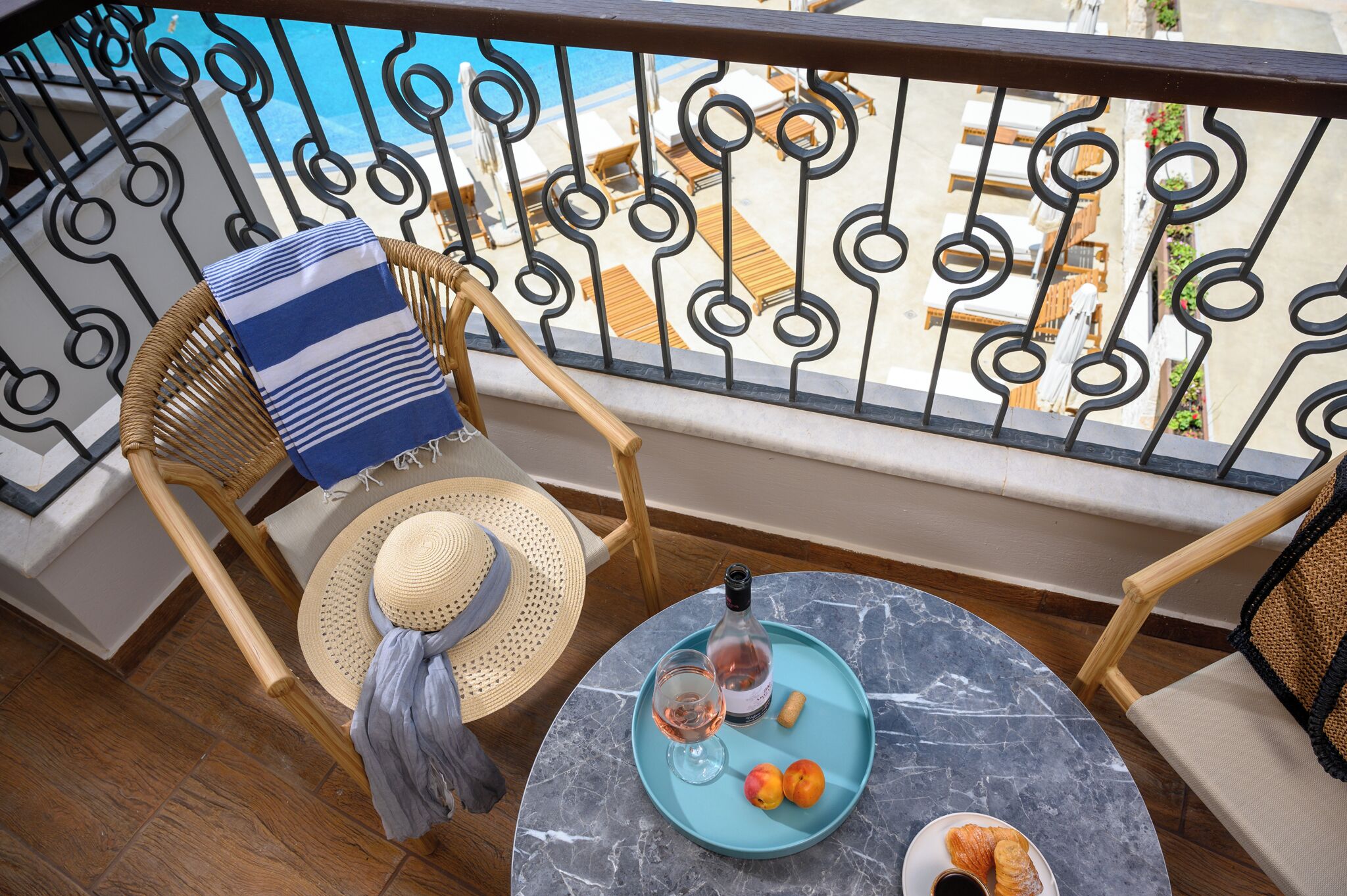 A balcony with wicker chairs, a table with a blue tray, a bottle, and a glass of wine.