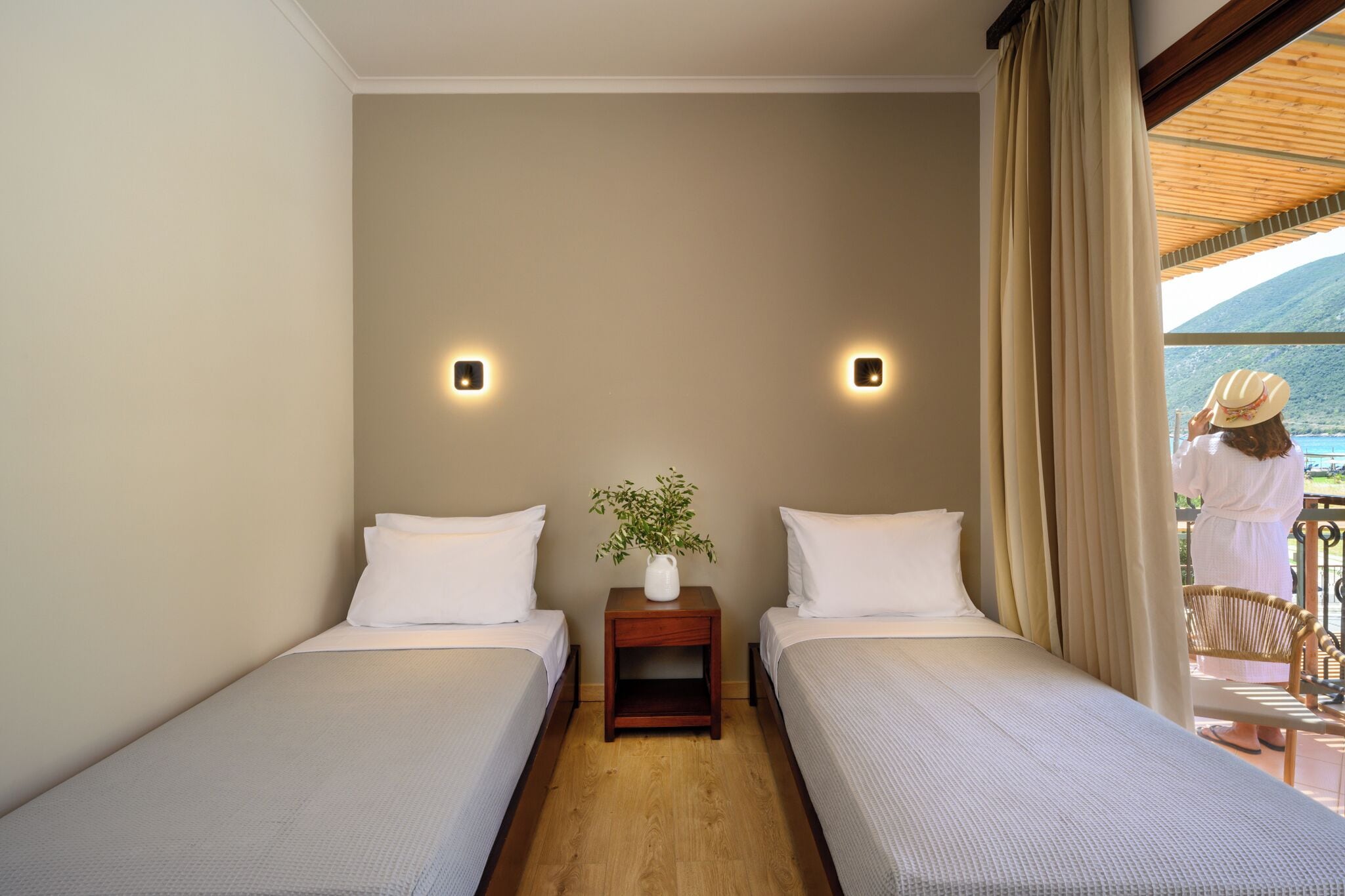 Ein Hotelzimmer mit zwei Einzelbetten, einem kleinen Nachttisch mit Pflanze und Blick ins Freie.