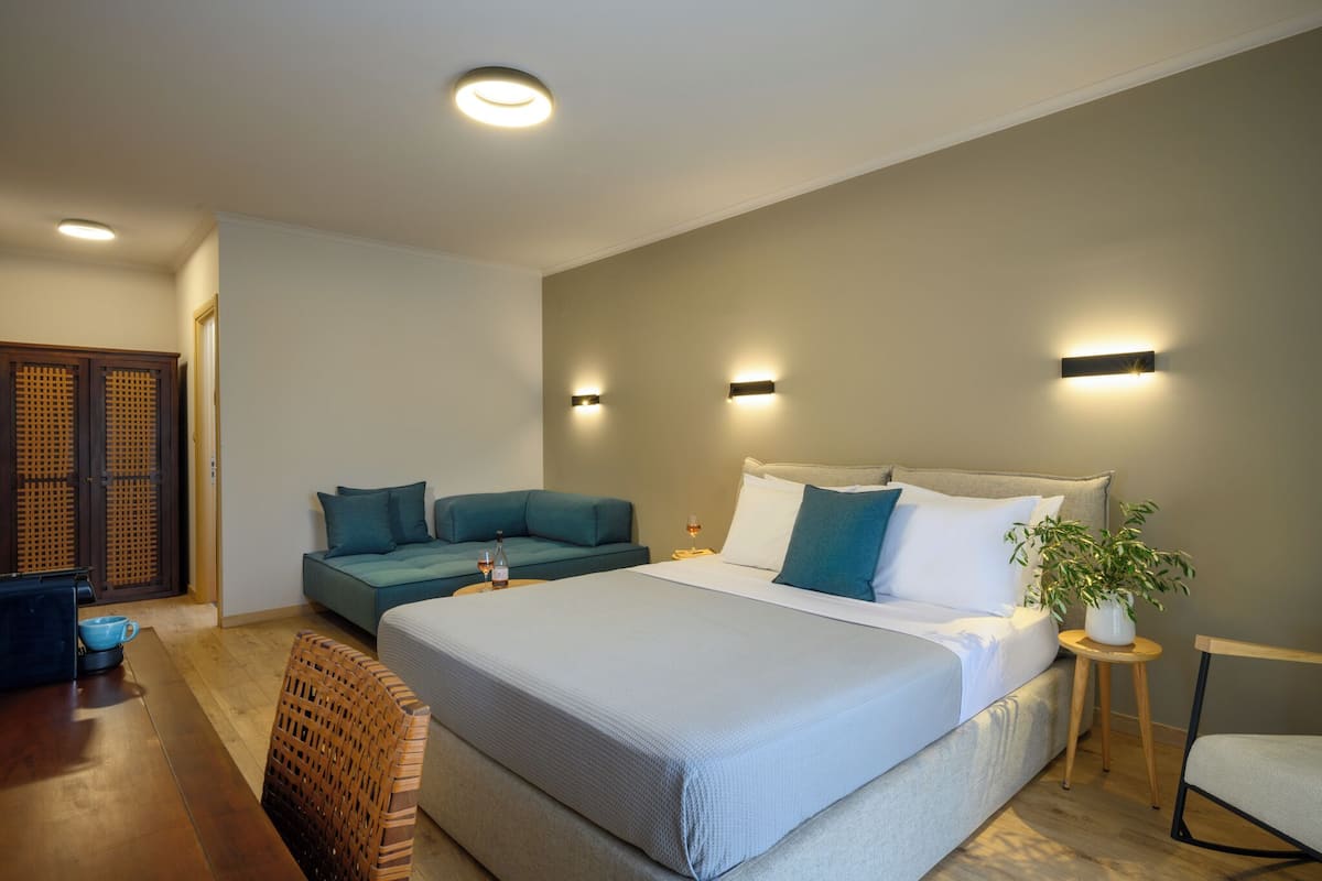A modern bedroom with a large bed, a sofa, a small table, and a potted plant.