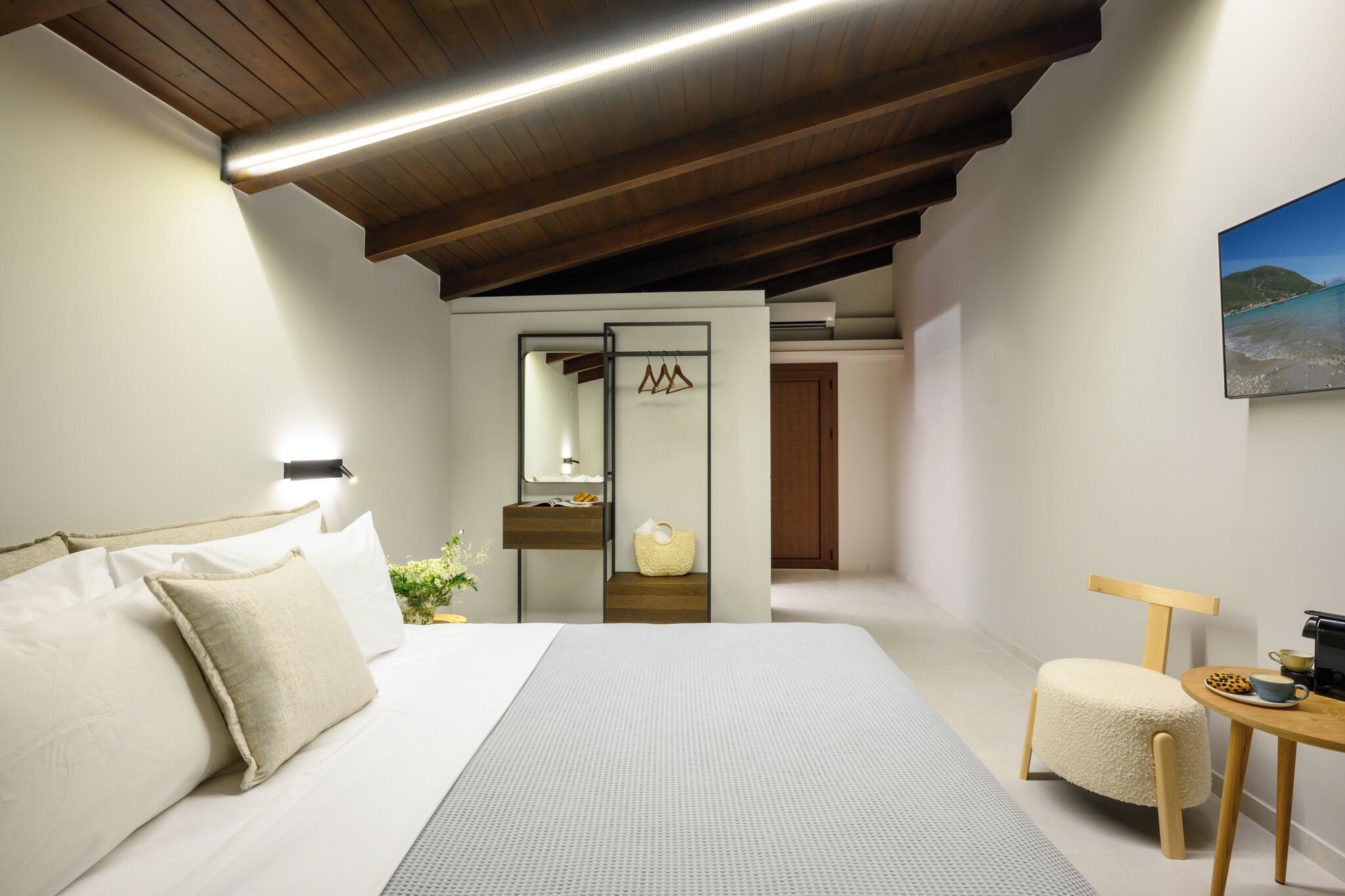 Um quarto com uma cama grande, teto de madeira, uma mesinha com uma xícara e uma cadeira.