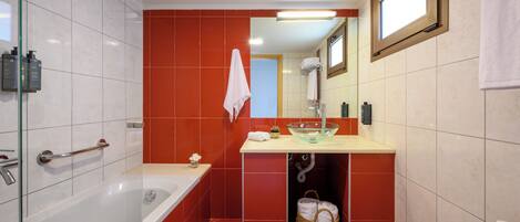 Un baño moderno con ducha de vidrio, una bañera blanca, un lavabo beige con lavamanos de cristal y paredes de azulejos rojos.