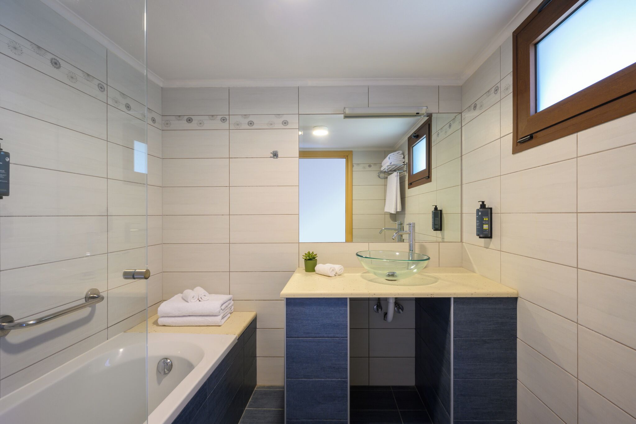 Een moderne badkamer met een glazen inloopbad, een wastafel met glazen kom en een handdoekrek.
