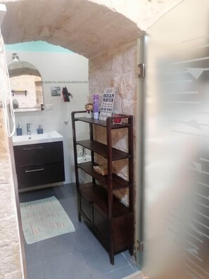 A bathroom with a white sink, dark wooden vanity, and a shelf with toiletries. - Gorgeous stone built apartment in the heart of Giovinazzo's historic center (Giovinazzo)