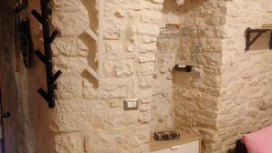 Una habitación con pared de piedra, un armario blanco, una cama rosa y una pequeña estantería con vasos.