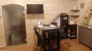 Una cocina compacta con pared de piedra, un televisor de pantalla plana, cafetera y pileta.