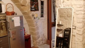 Una cocina con pared de piedra, un refrigerador, una cesta y un estante con botellas.
