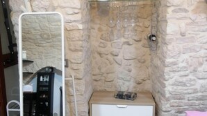 Una habitación con pared de piedra, un aparador blanco, un espejo y una estantería con vasos.