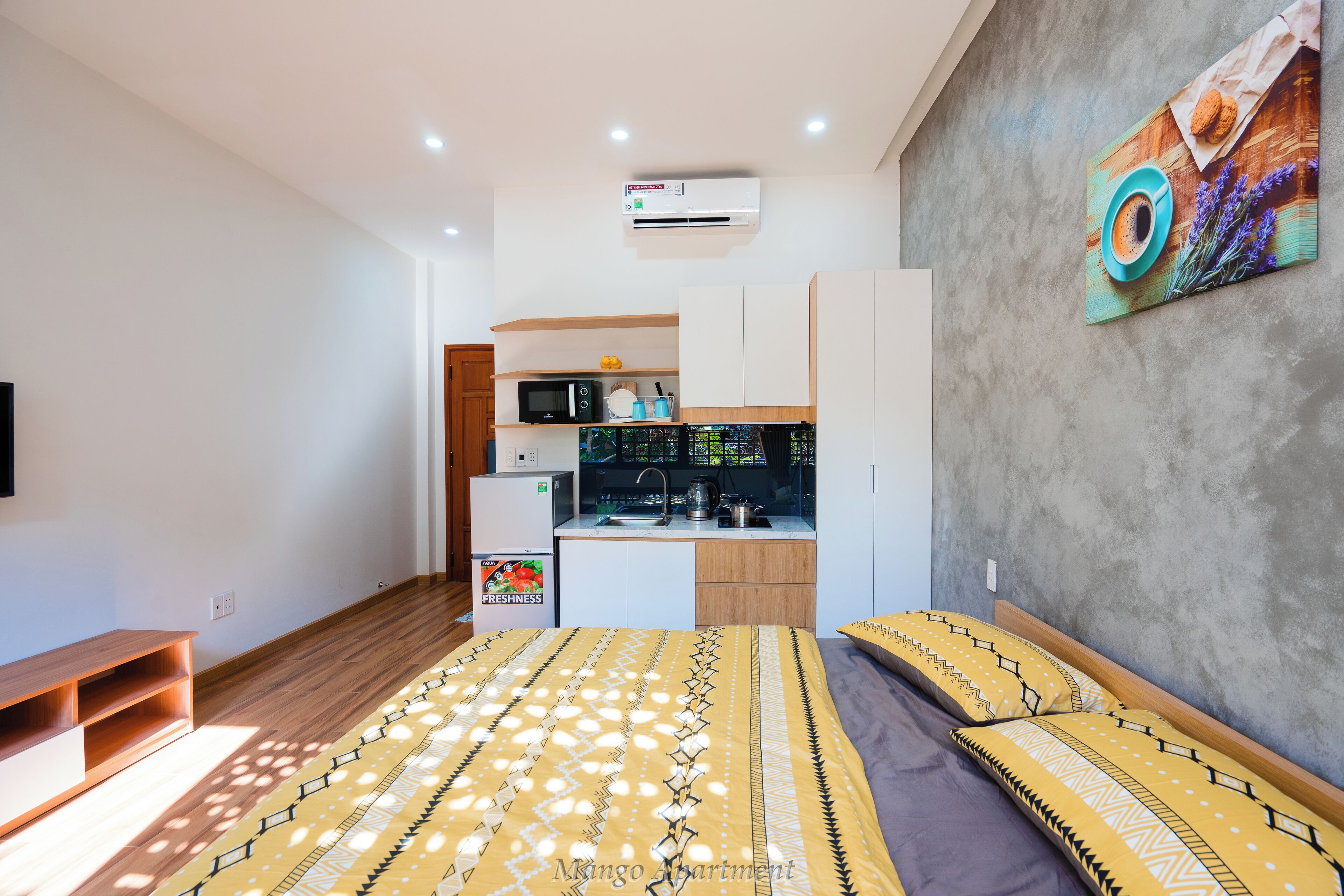 A compact bedroom with a bed, a small kitchenette, and a mounted air conditioner.