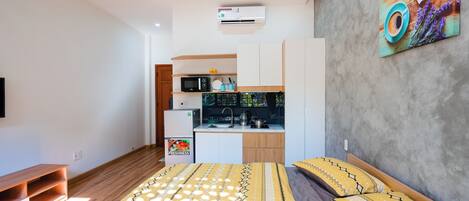 A compact bedroom with a bed, a small kitchenette, and a mounted air conditioner.