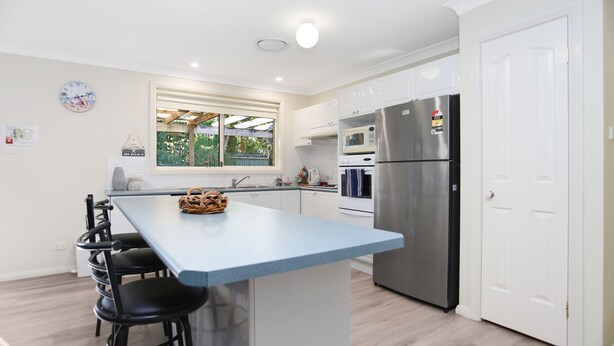 Una cocina moderna con armarios blancos, un refrigerador de acero inoxidable y una isla grande con taburetes de bar.