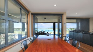 A spacious dining area with a long wooden table, surrounded by chairs, leading to a balcony with a view of the sea.