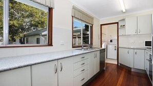 A modern kitchen with white cabinets, a stainless steel sink, and a built-in dishwasher. - Stroll To Bennett's Beach (Hawks Nest)