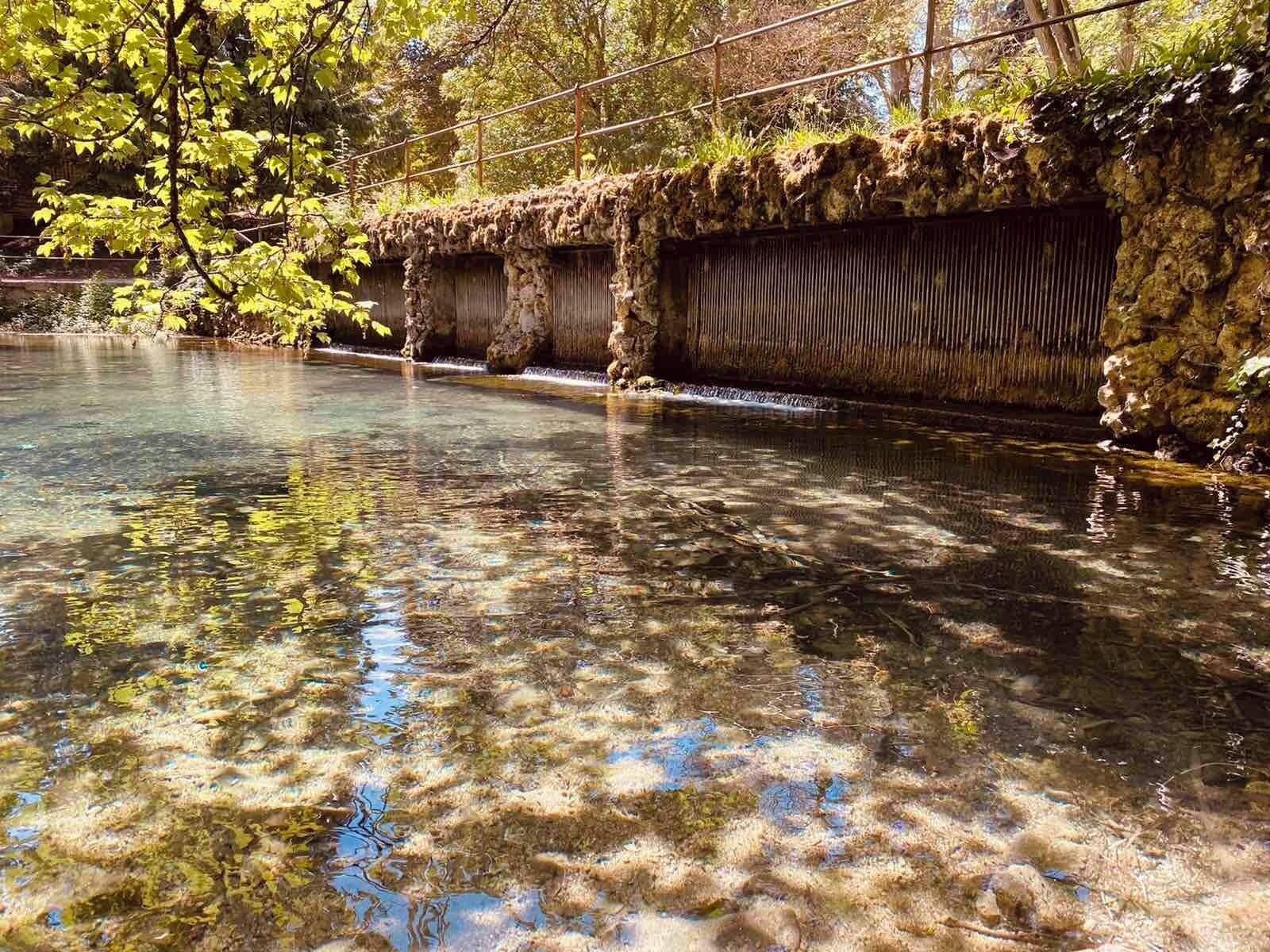 Un plan d’eau aux eaux claires, avec une formation rocheuse et des arbres en arrière-plan.