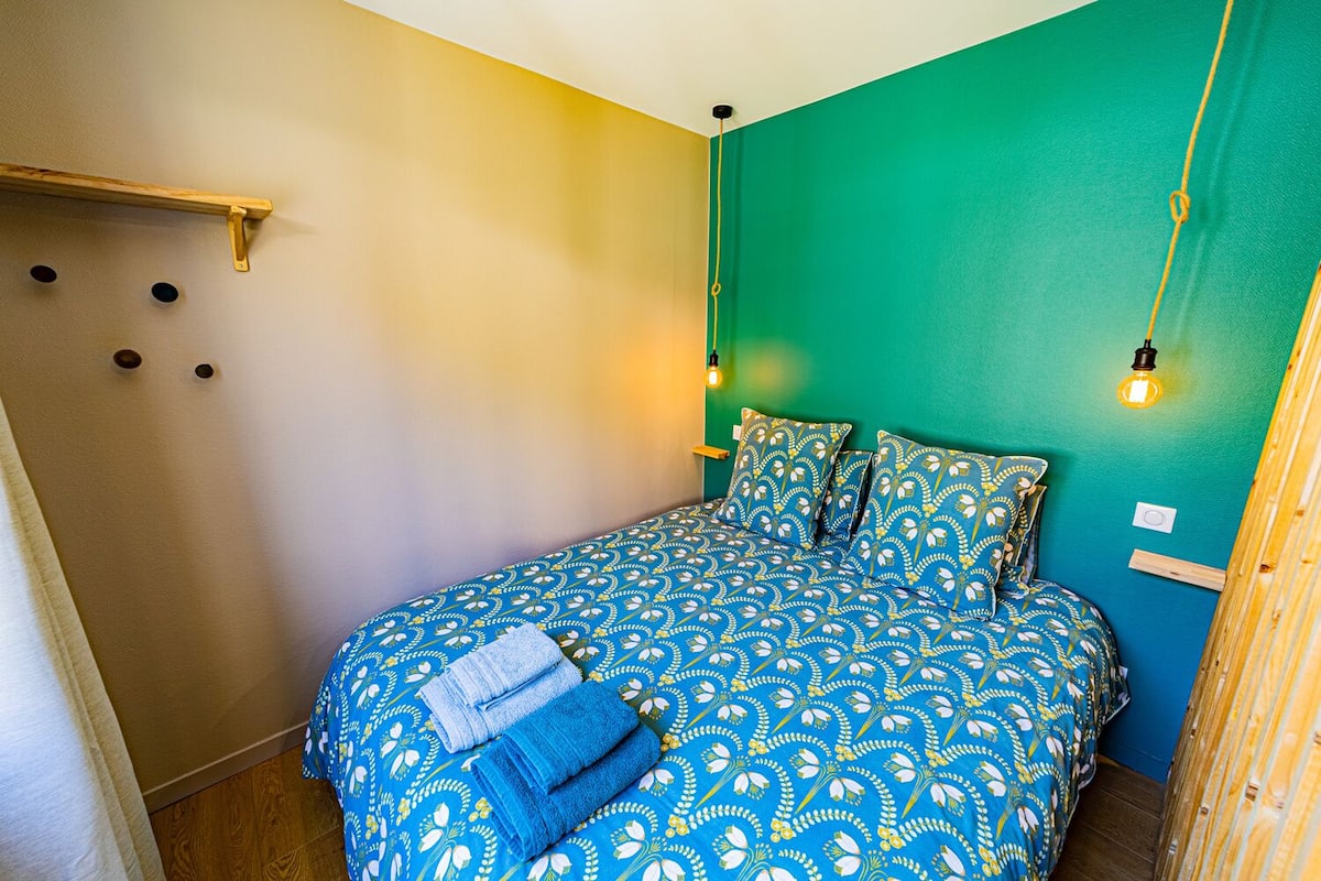 A bed with a blue patterned bedspread and pillows, a wooden headboard, and two wall-mounted light fixtures.