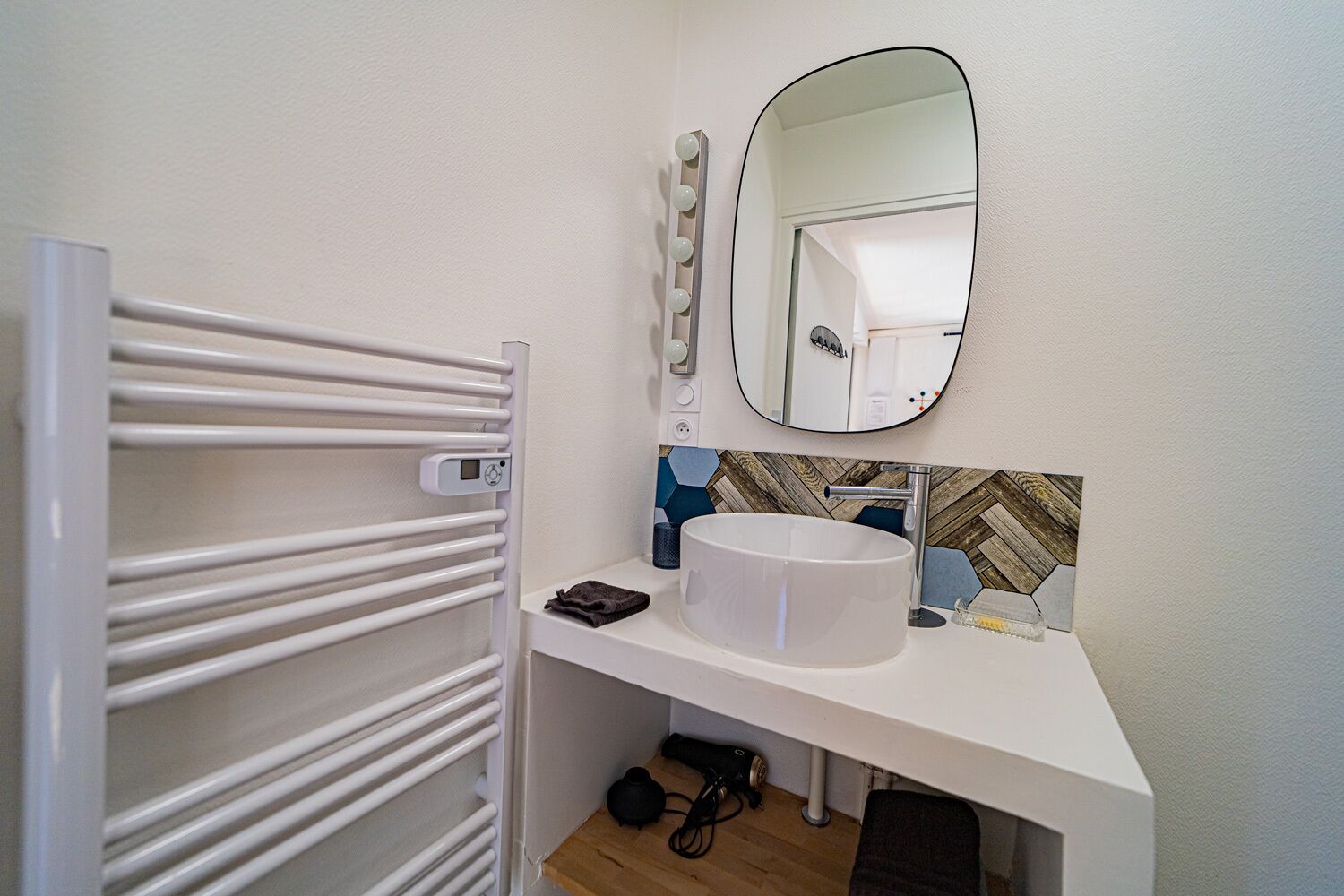 A bathroom with a white sink, a mirror with lights, a towel, and a heater.