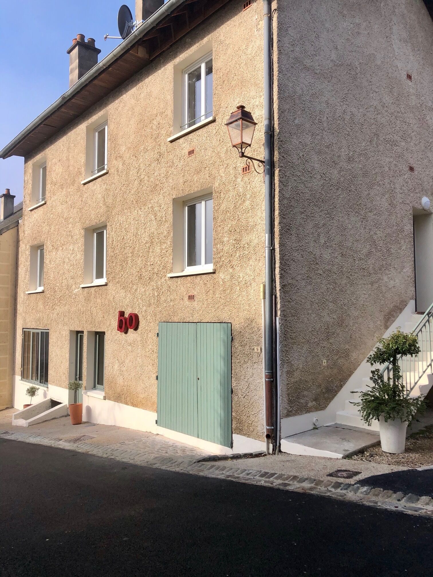 Edificio de dos pisos con fachada texturizada, número 60, que presenta una puerta verde, varias ventanas y una pequeña escalera que conduce a un nivel superior.