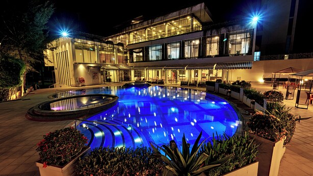 A modern hotel with a large outdoor swimming pool, well-lit surroundings, and a multi-story structure. - Insignia Hotels & Resorts (Tongi)