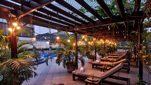 An outdoor lounge area with wooden benches, potted plants, and string lights. - Insignia Hotels & Resorts (Tongi)