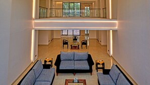 A spacious interior with a high ceiling and a glass roof, featuring a central seating area with sofas and a coffee table. - Insignia Hotels & Resorts (Tongi)