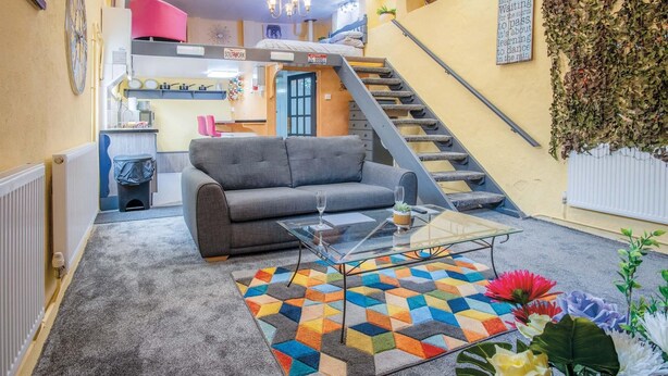A living room with a sofa, a glass coffee table, and a colorful rug. There is a staircase leading to an upper level. - Clouds - 1 Bedroom Holiday Home - Milford Haven (Milford Haven)