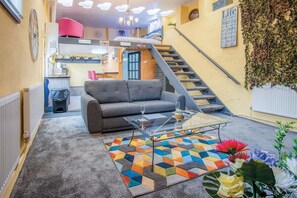 A living room with a sofa, a glass coffee table, and a colorful rug. There is a staircase leading to an upper level. - Clouds - 1 Bedroom Holiday Home - Milford Haven (Milford Haven)